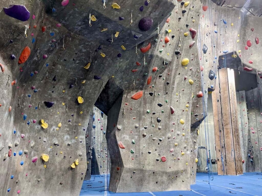 Rock climbing wall at indoor climbing gym with holds bolted to wall and ropes hanging down