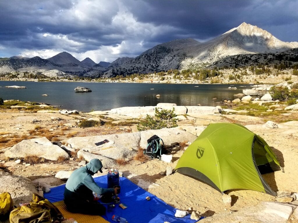 A man makes supplies next to his tent on the Minarets Lake Loop on the John Muir Trail