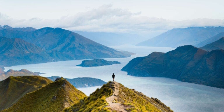 Man standing at Roys Peak viewpoint on the South Island of New Zealand with stunning views of fjord and mountains