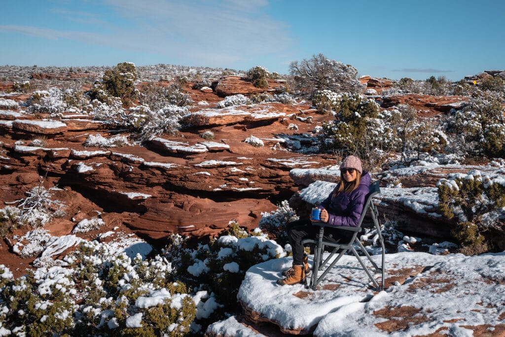 A woman sits on a YETI Trailhead Camp chair among snow-covered red rocks in Moab, Utah