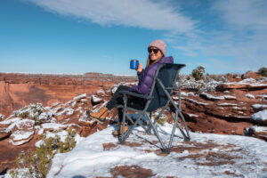 Woman sitting on the YETI Trailhead Camp Chair in a snowy, scenic red rock location in Utah