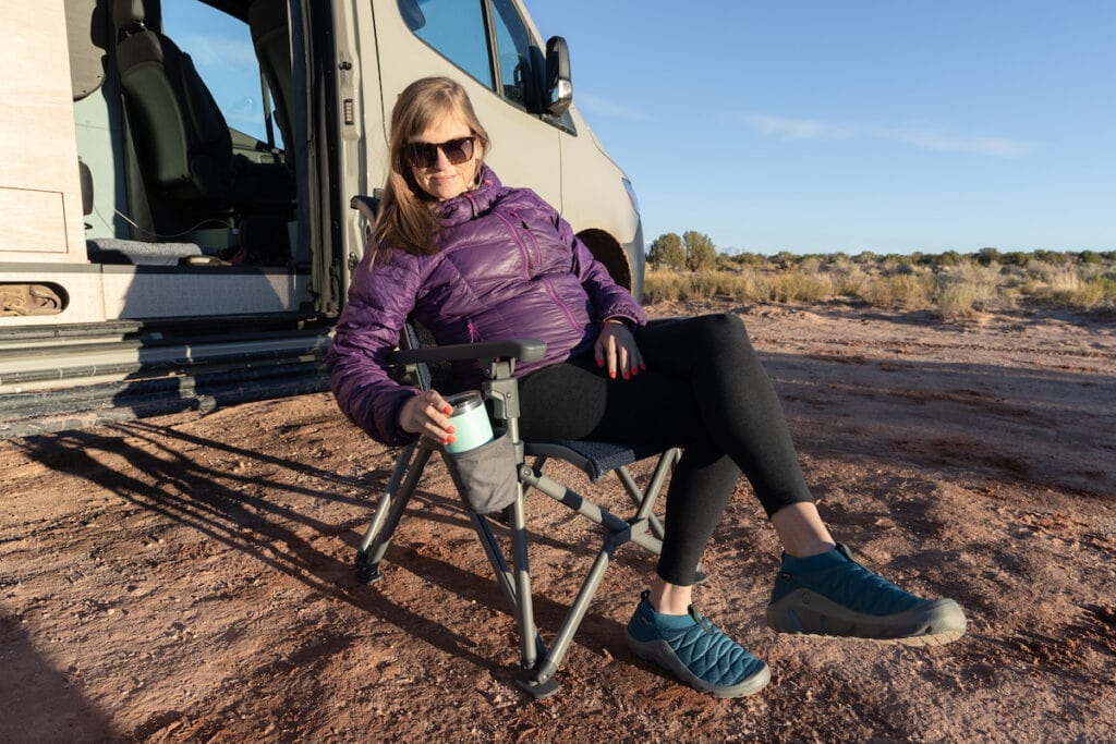 A woman places an insulated cup in the YETI Trailhead Camp chair cup holder