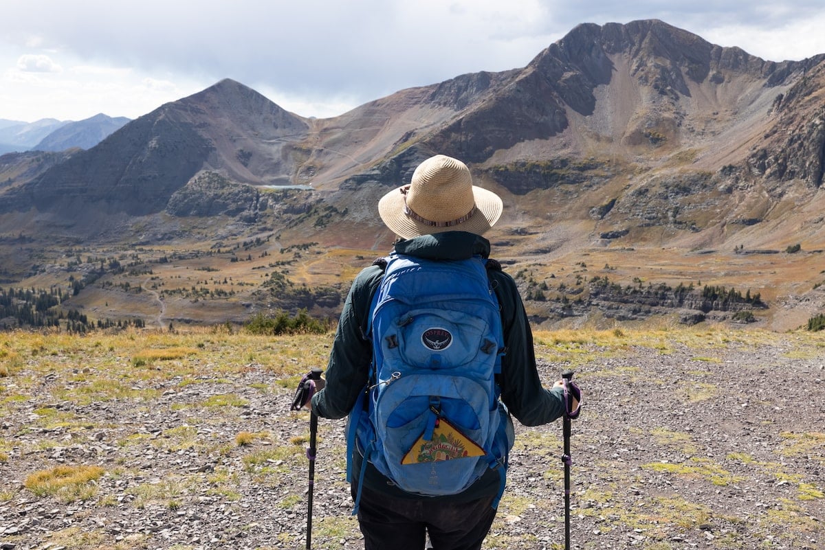 Woman hiker with her back to the camera wearing a daypack and hat