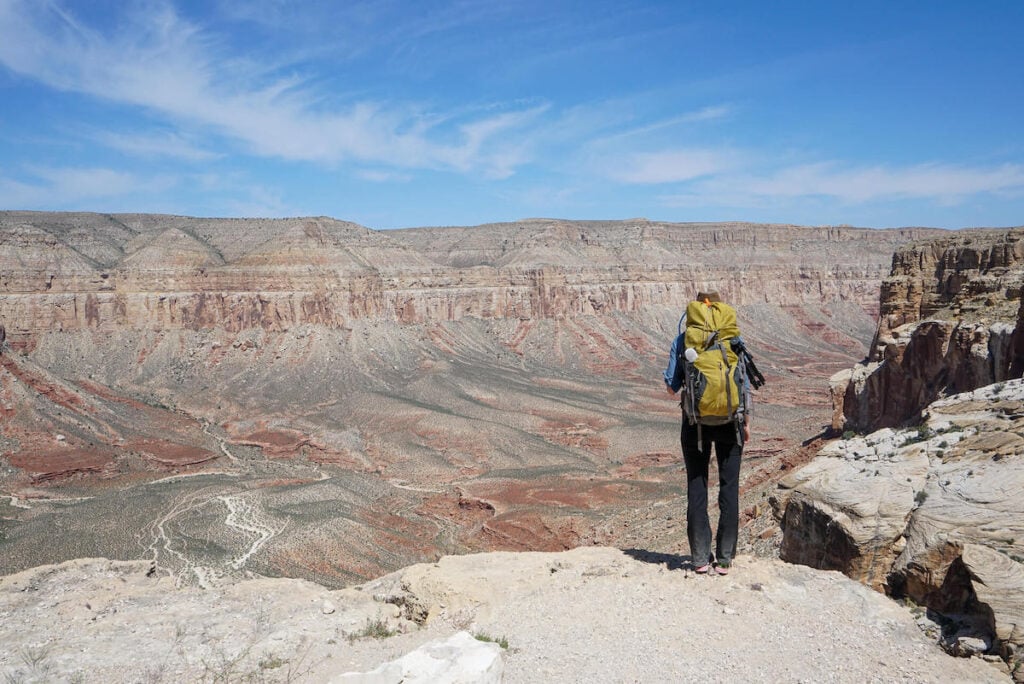 A person wearing a yellow backpacking pack stands near the top of Havasu Canyon before hiking down