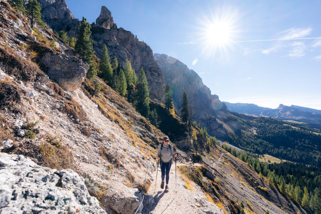 Woman hiking on a trail along a sunny slope with mountains and trees in the background