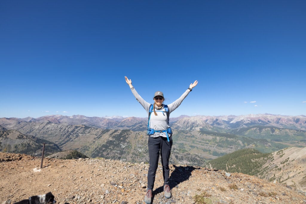 Kristen posing for photo on hiking trail in Colorado with both arms outstretched overhead