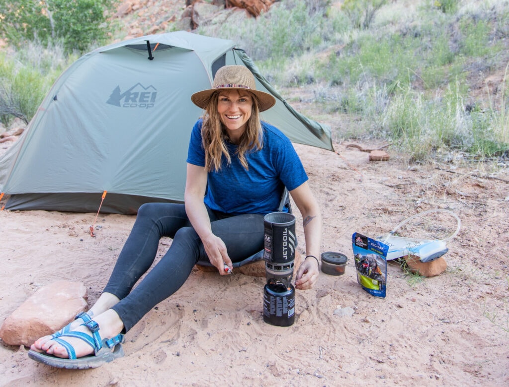 Bearfoot Theory outdoor blog founder Kristen sitting on the ground making dinner in front of a tent on a backpacking trip