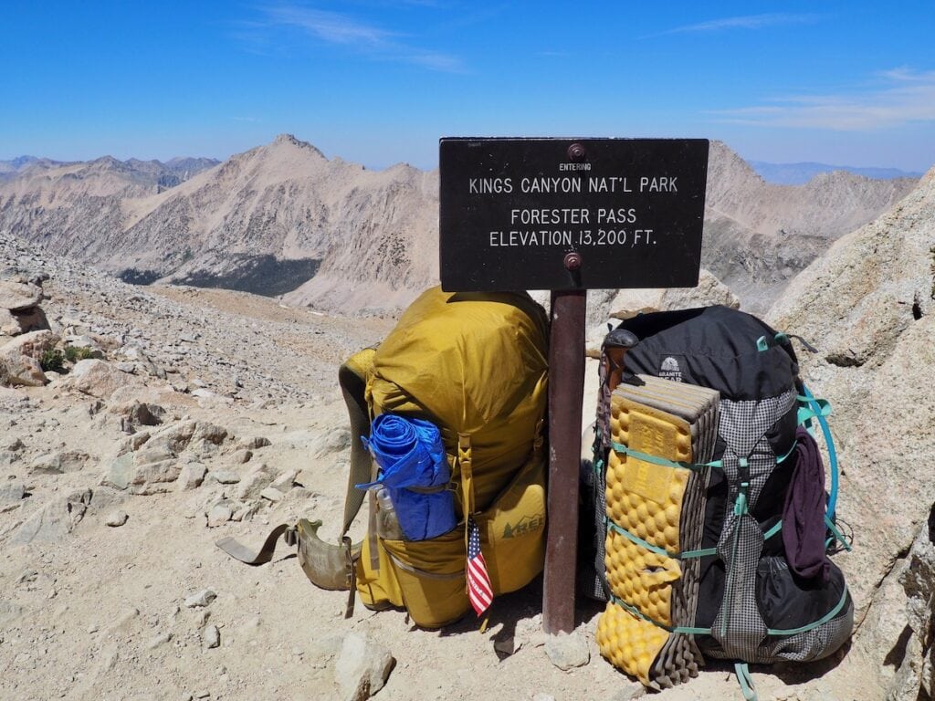 Two backpacking packs leaned versus an "entering Kings pass National Park" sign at the top of Forester Pass