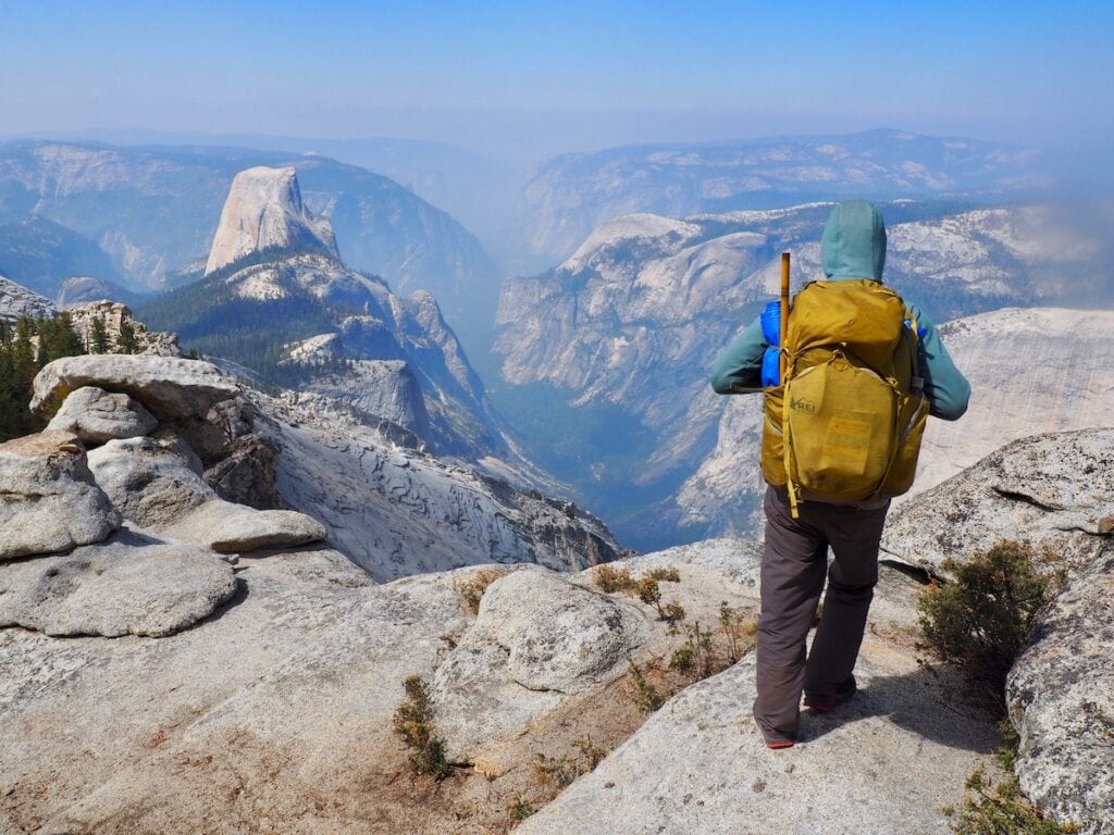 A man stands at the summit of Cloud's Rest in Yosemite overlooking Half Dome