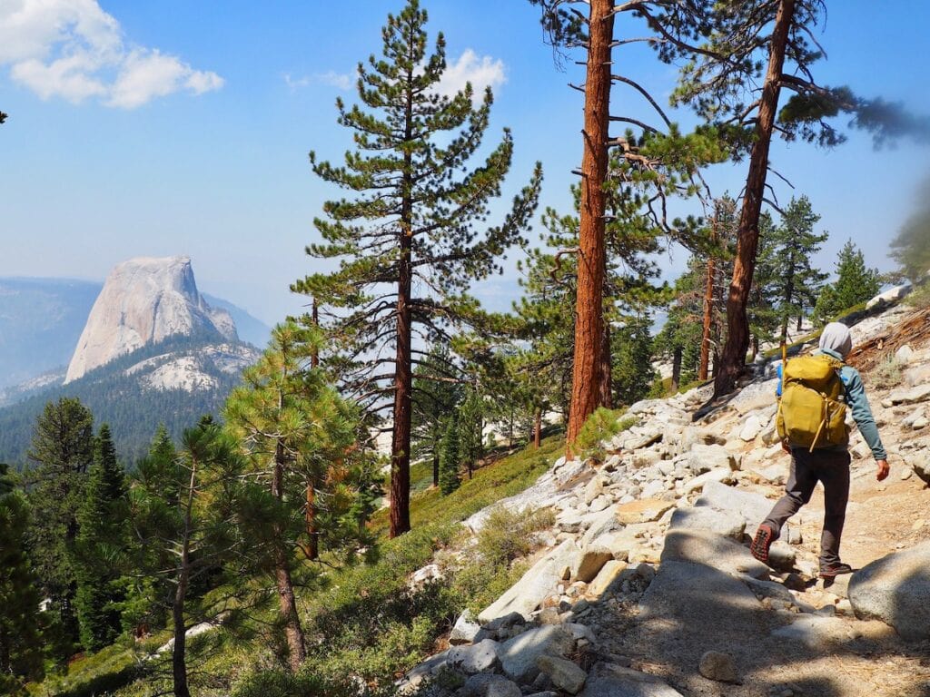 View of Half Dome from the John Muir Trail. A man wearing a yellow walkabout hikes on the trail.