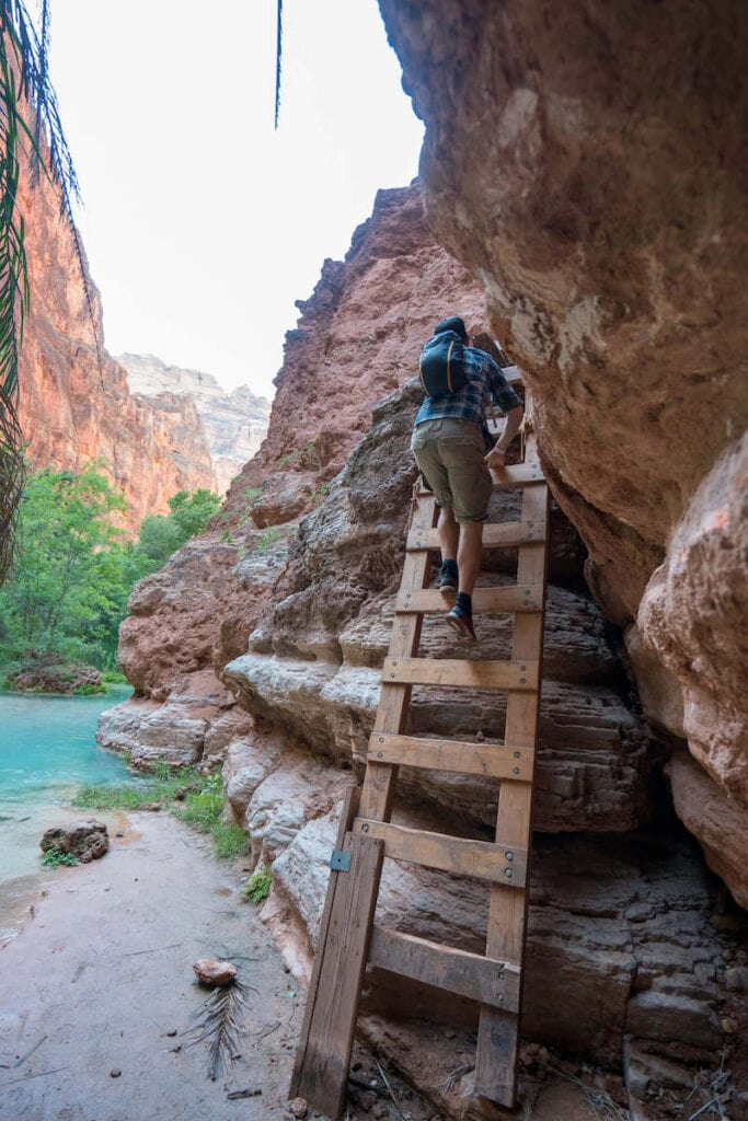 Man climbing down wooden ladder to Mooney Falls in Havasupai Arizona