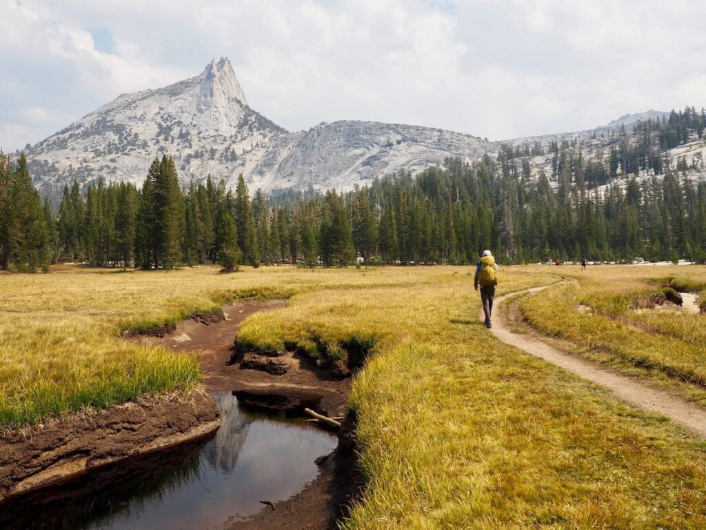 A man hikes in a flat meadow along the Lower Lake Trail through the John Muir Trail