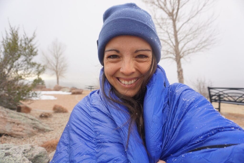 Woman taking a selfie wrapped up in Outdoor Vitals Summit down sleeping bag during light snow fall