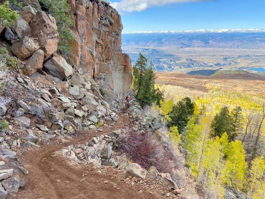 Mountain biker riding down steep, narrow Palisade Plunge Mountain Bike Trail with drop-off to the right
