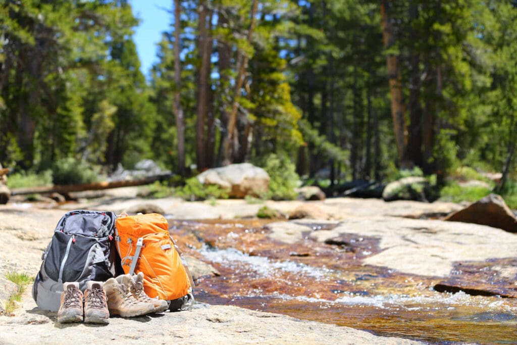 Two ultralight backpacking backpacks and two pairs of shoes on rocks near river