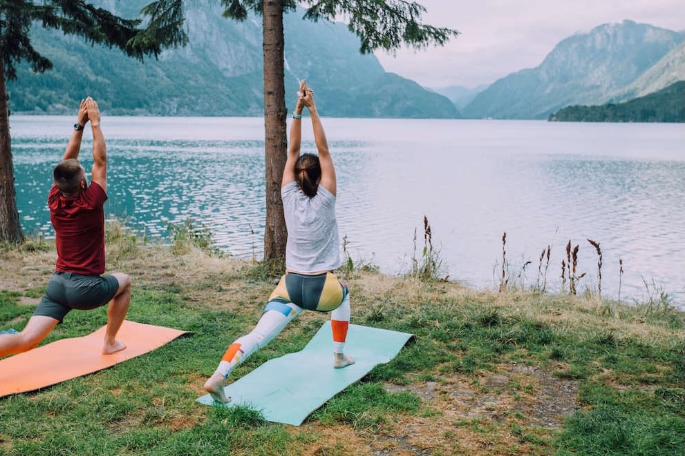 Two people doing yoga next to lake and mountains 