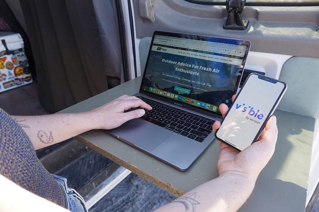 Closeup of woman working on her laptop with the Visible Wireless logo on her cell phone