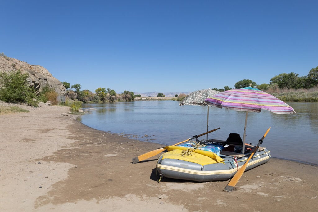 Packraft loaded with gear and shaded with two unbrellas pulled up on beach on Colorado River