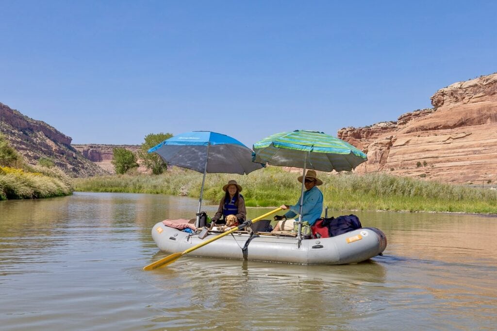 Two people sitting in packraft on Colorado River with two umbrella shading them from the sun