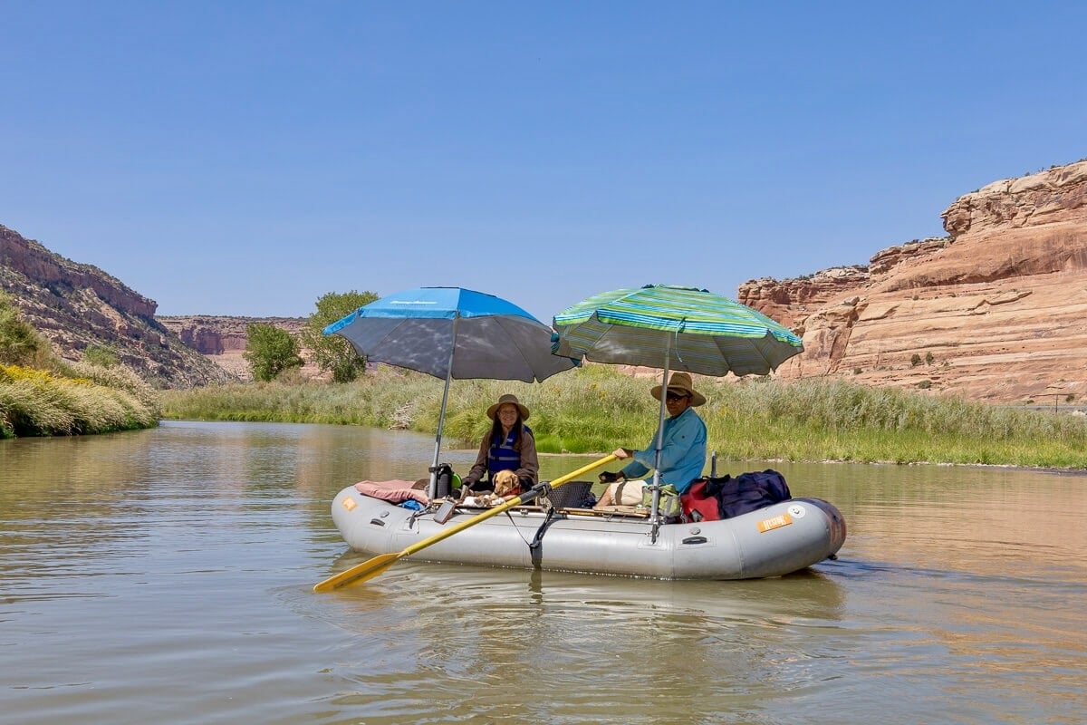 Two people in packraft on the Colorado River in Utah with two umbrellas providing shade