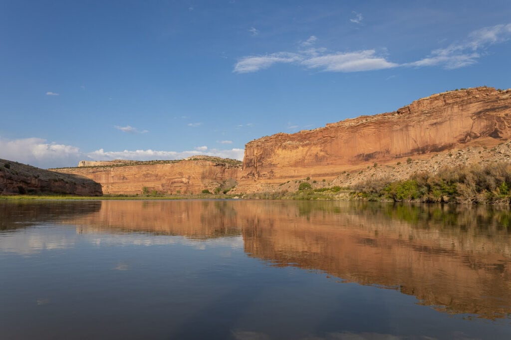 Tall red rock bluffs rising up from water on the Colorado River in Utah through Ruby-Horsethief Canyon