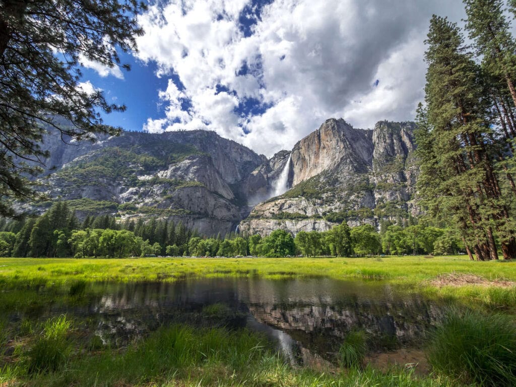 Waterfall in Yosemite National Park with lake and meadow in foreground