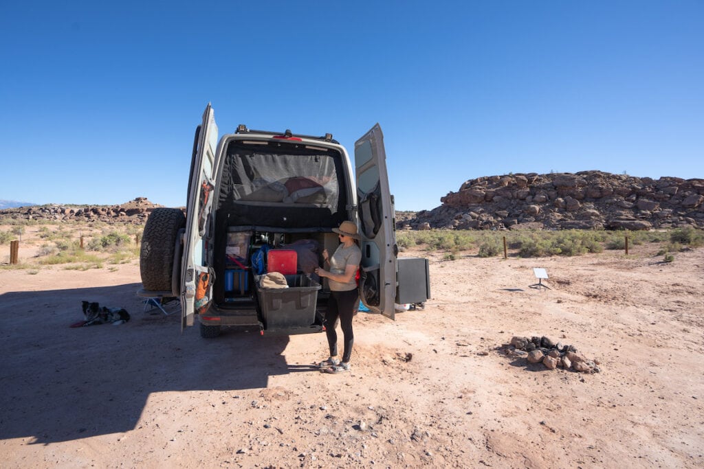 A woman stands outside of a Sprinter van with the back doors  open