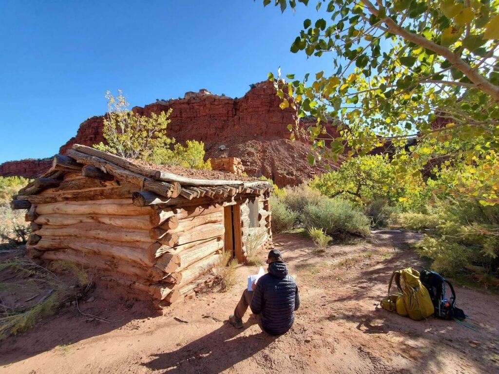 Hiker sitting in front of restored Hackberry cabin on hike in Grand Staircase-Escalante National Monument in Utah