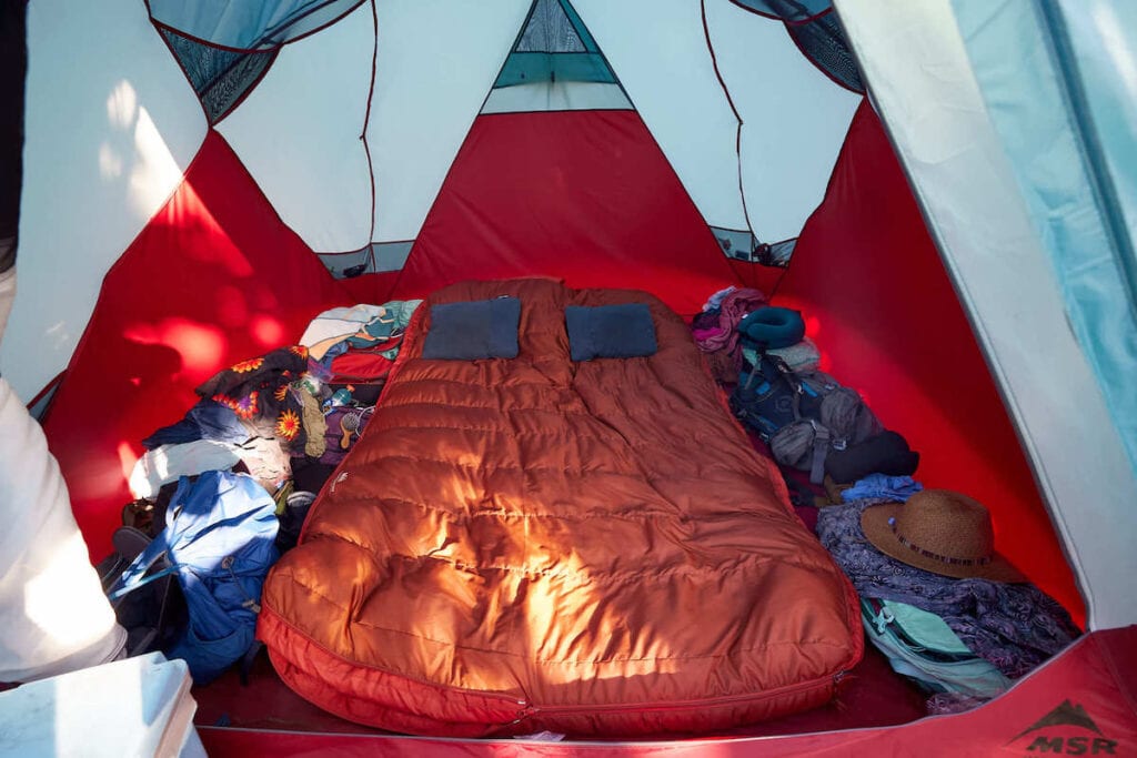 Double sleeping bag and sleeping pad in erected tent with camping gear spread out around it