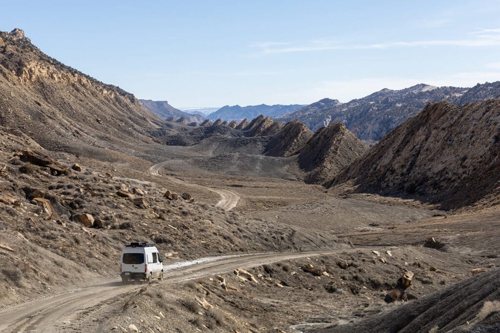 The Storyteller Overland Classic MODE AWD van driving off-road on a muddy dirt road through a Mars-like landscape in Southern Utah