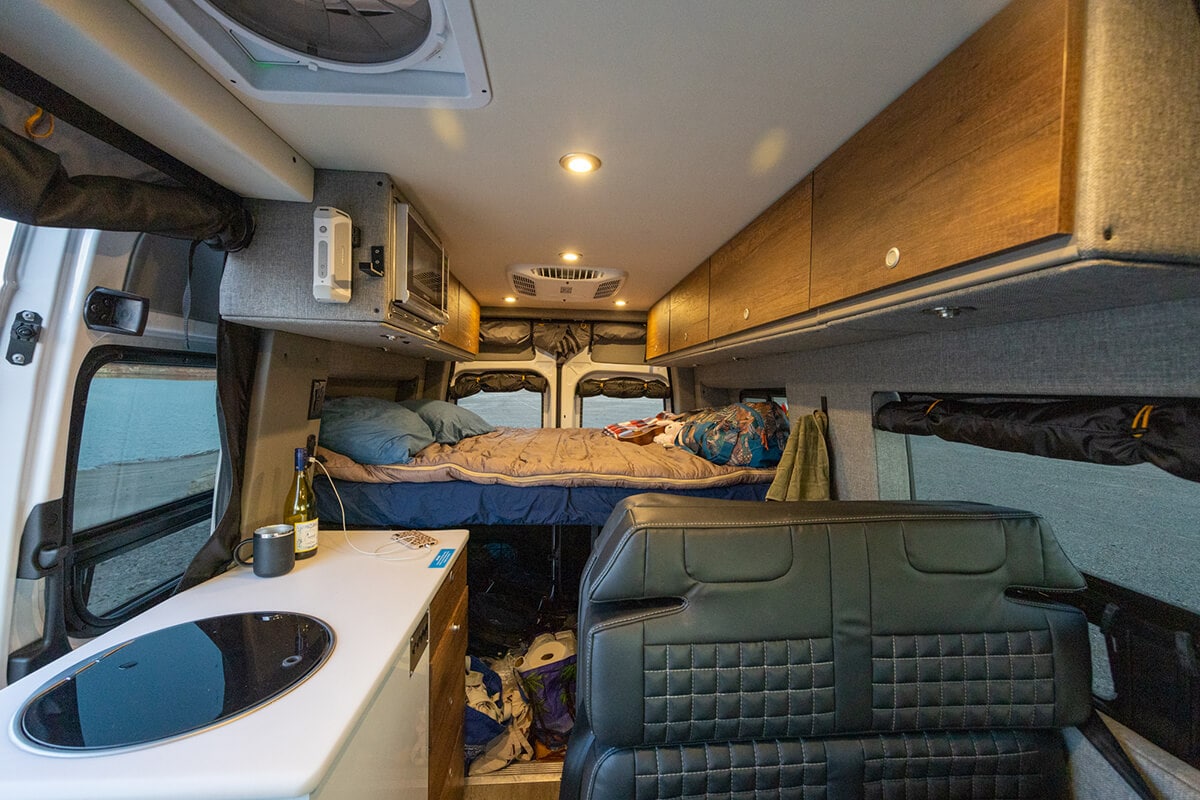 Interior of the Storyteller Overland Classic MODE van showing the galley/kitchen, bed, cabinets, and seating