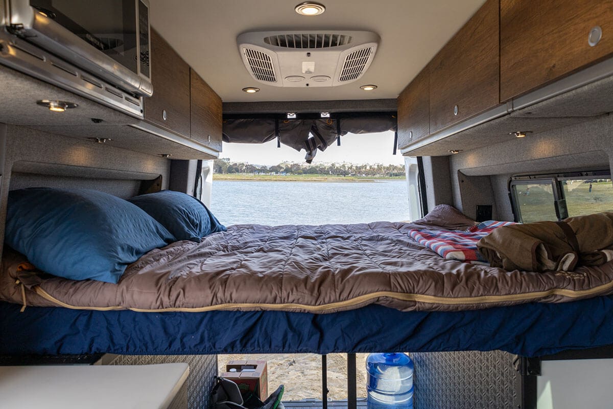 The main bed inside the Storyteller Overland Classic MODE van set up with pillows and a sleeping bag