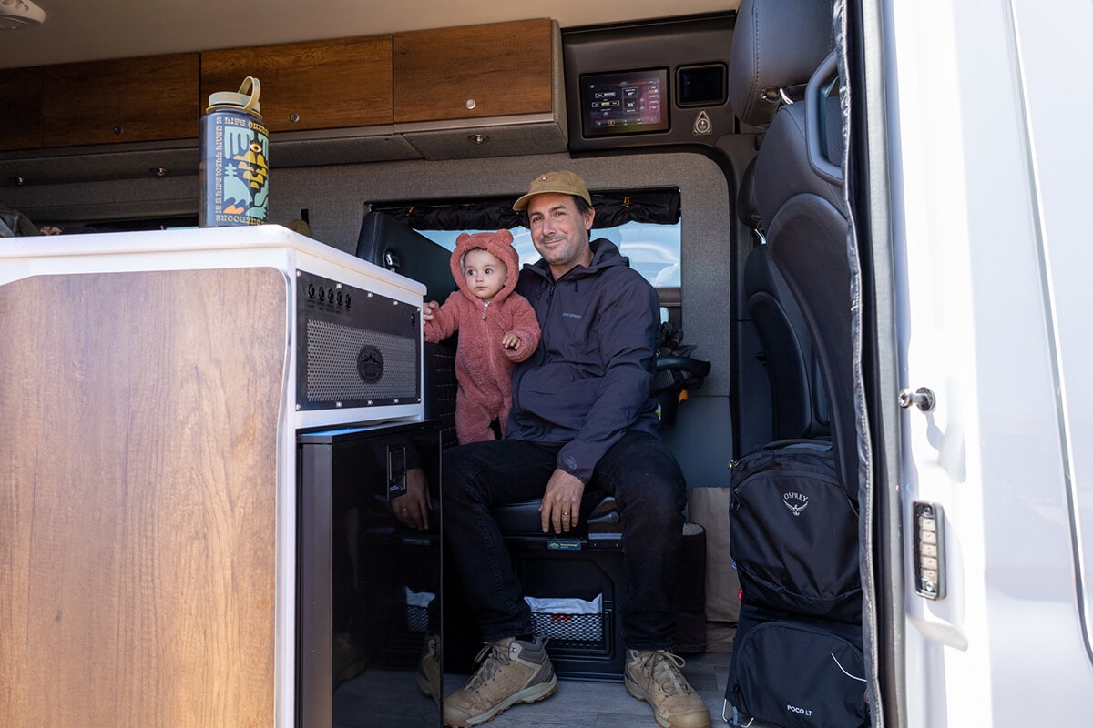 A man holding his toddler sitting inside the Storyteller Overland Classic MODE van with the control panel above