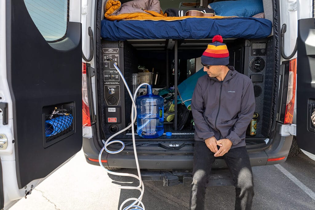 Filling up the water tank in the back garage of the Storyteller Overland Classic MODE van using the siphon feature