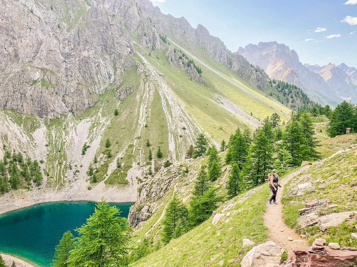 Woman on hiking trail in Italy carry child in backpack surrounded by Alp landscapes and high alpine lake