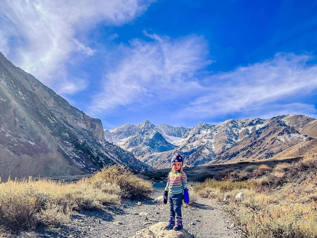 Little girl on hiking trail with towering snow-capped Eastern Sierra mountains behind her