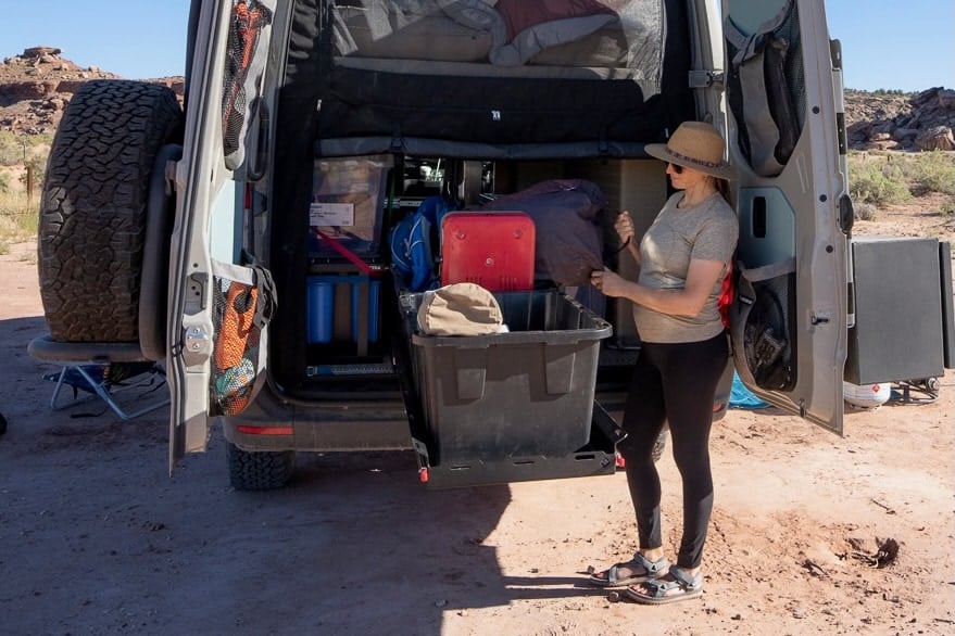 Woman standing at back of converted Sprinter Van with back doors open to gear storage