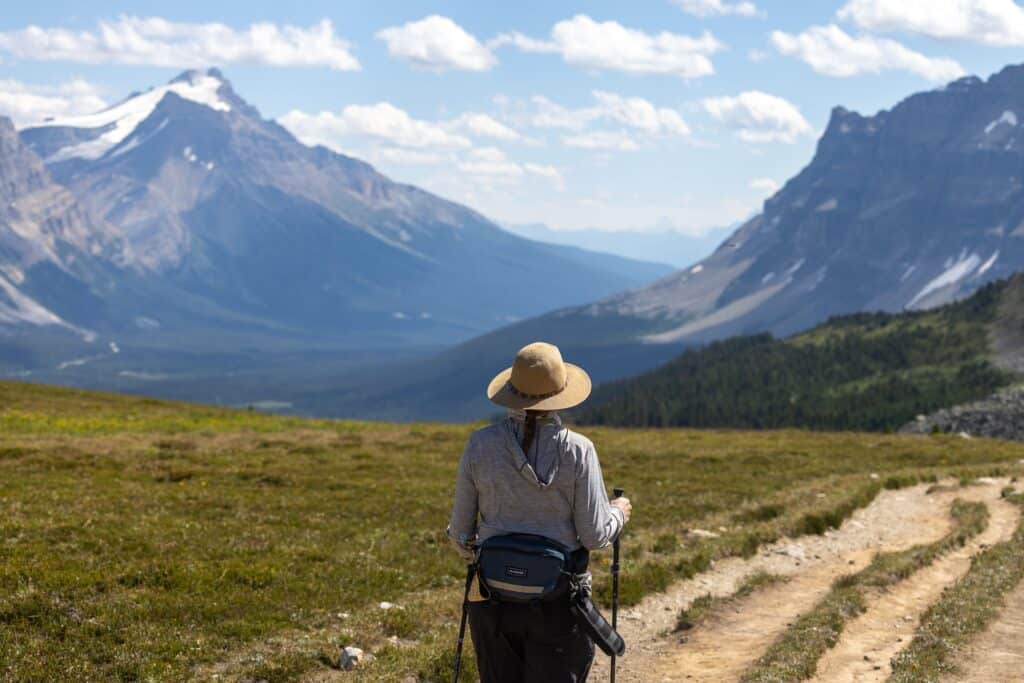 Back of woman hiking with mountains in the background. a can of bear spray is hanging from her hiking fanny pack