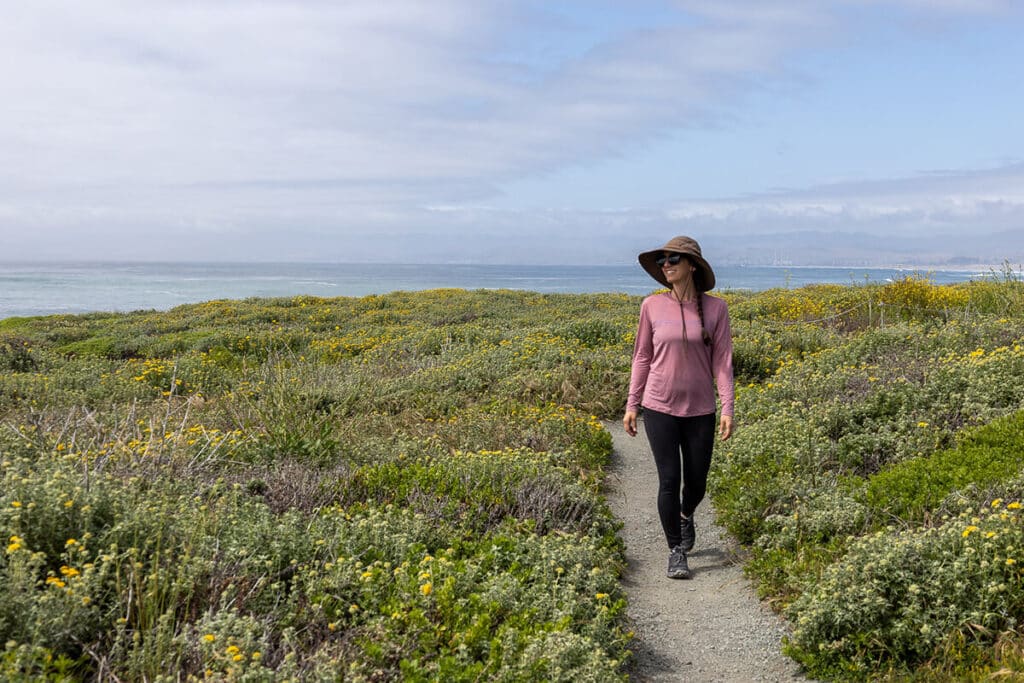 Woman hiking in the Oboz Katabatic shoes through a field of flowers with the ocean in the preliminaries in Montana de Oro State Park