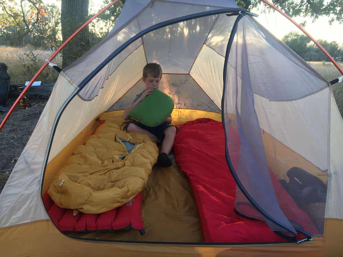 Kid blowing up inflatable pillow in tent next to sleeping bags