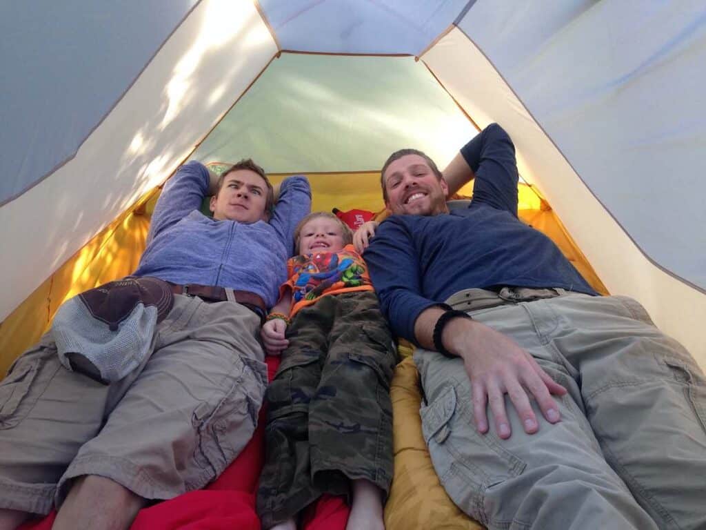 Man and two kids lying side by side in camping tent