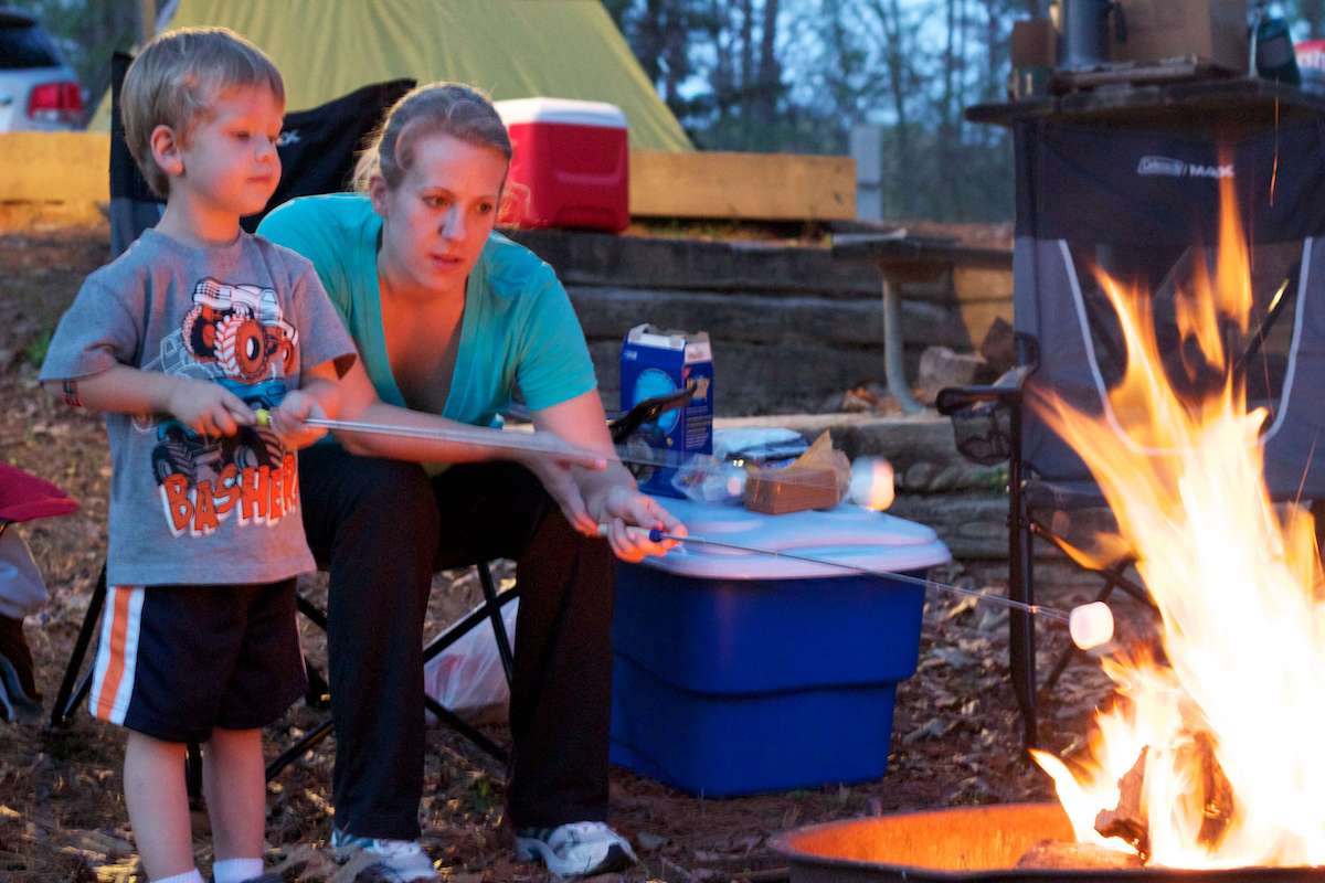 Child and mother roasting marshmallows on campfire at campsite