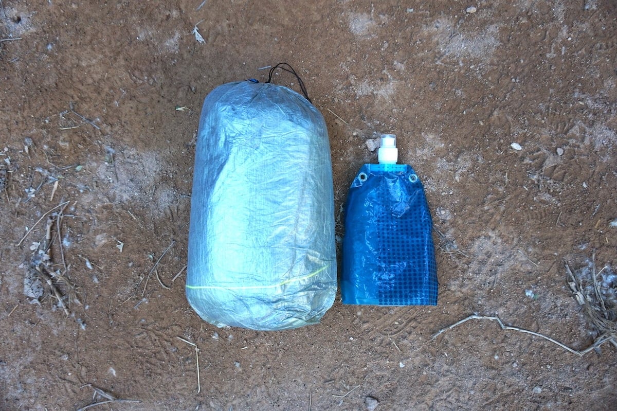 Zpacks Duplex tent in its stuff sack laying out on the ground next to a 1L soft waterbottle