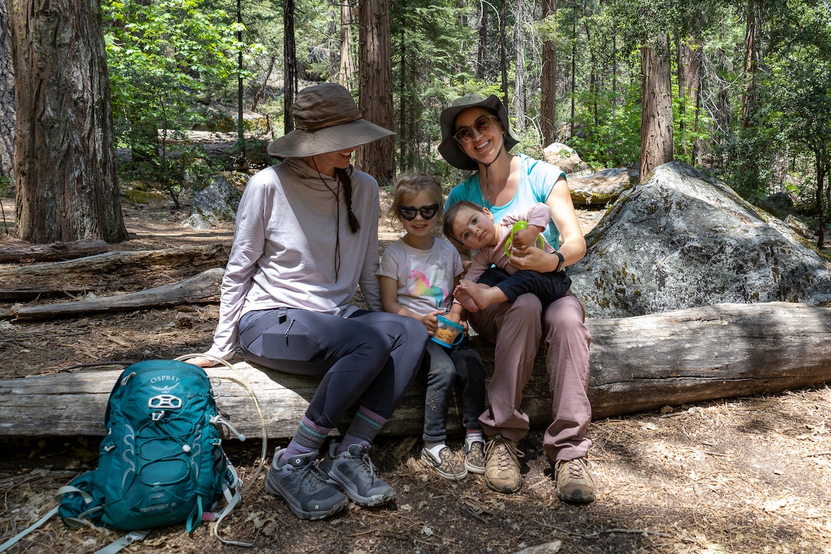 two adult women sit on a log in Yosemite with two toddlers on their laps