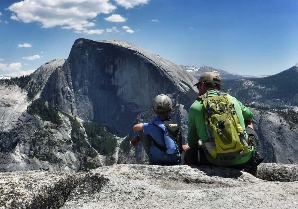 Father and son sitting at lookout point over Half Dome in Yosemite National Park