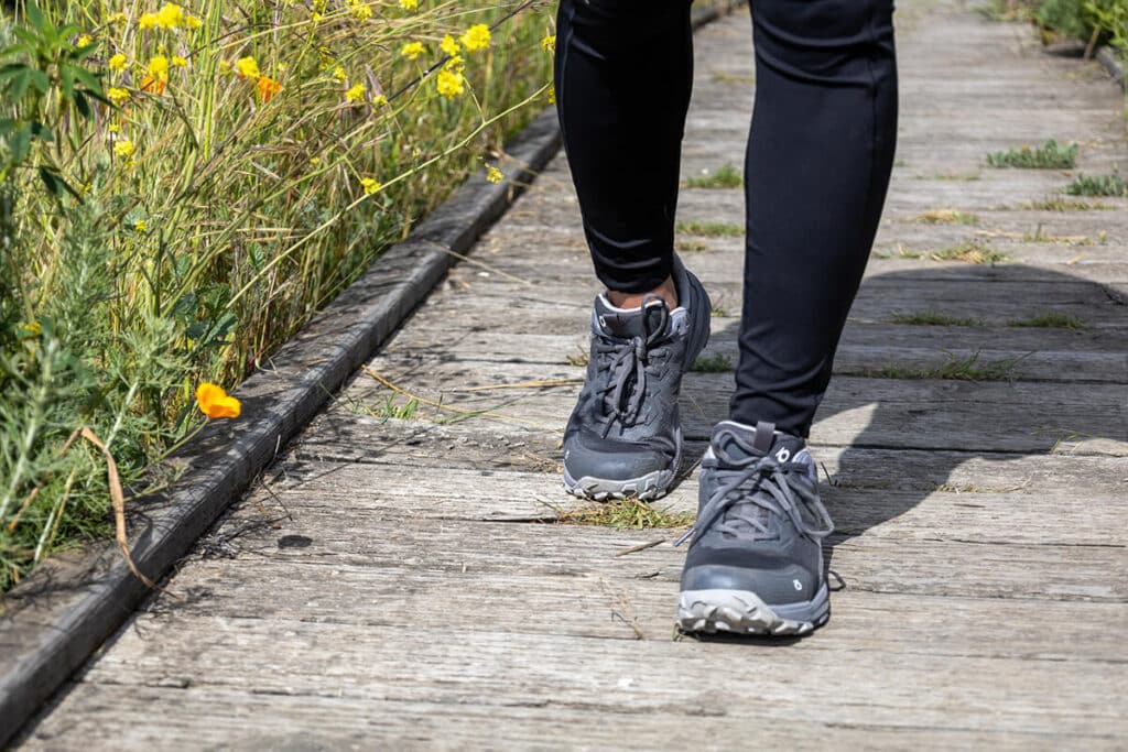 Closeup of the Oboz Katabatic hiking shoes on a wooden boardwalk trail with flowers in the background