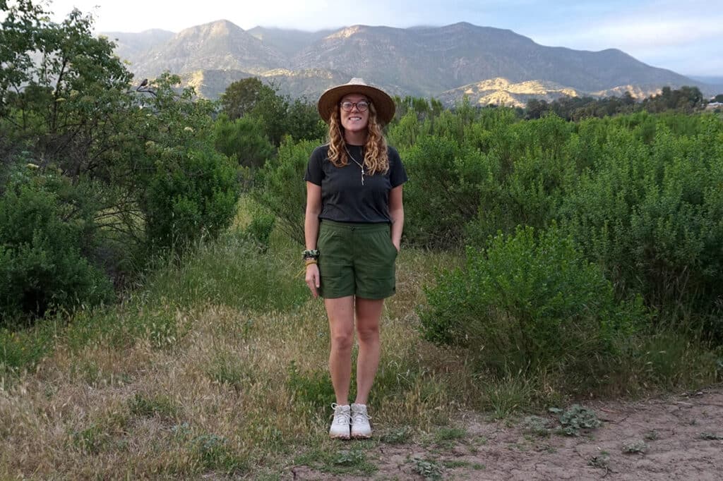 Woman traveler standing in front of a mountain background wearing the Oboz Katabatic hiking shoes and REI trailmade shorts