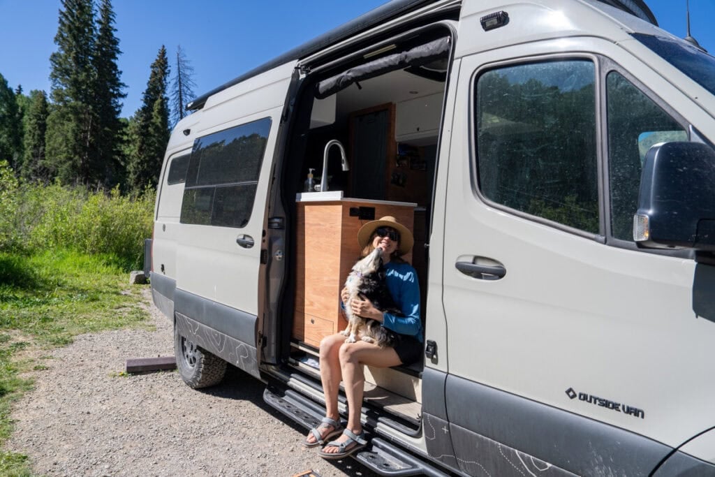 Kristen Bor sitting on the edge of a Sprinter Van with dog in her lap