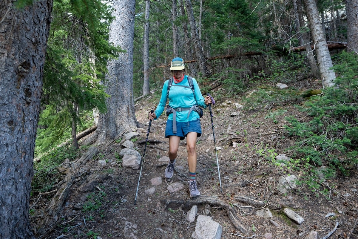 Kristen Bor hiking on a forested trail using hiking poles and wearing oboz katabatic lt hiking boots