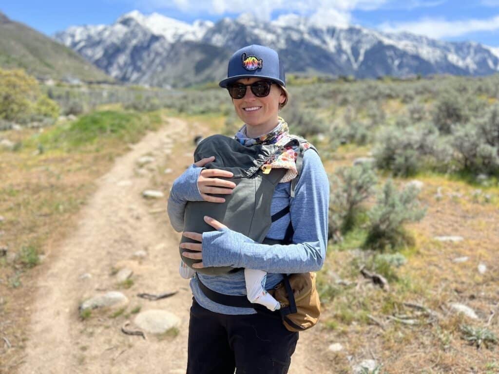 Woman smiles on a hiking trail in Salt Lake wearing a baby carrier and Costa Long Sleeve Venture Performance Shirt